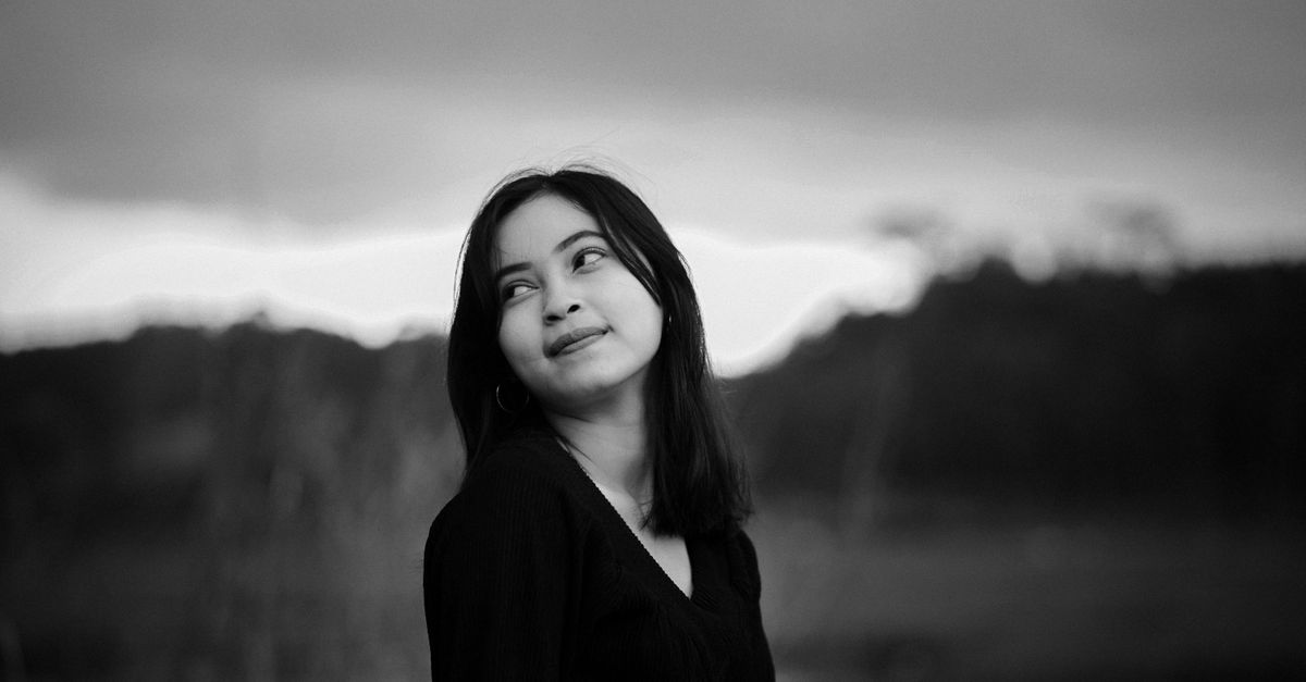 A captivating black and white portrait of a young woman looking upwards outdoors.